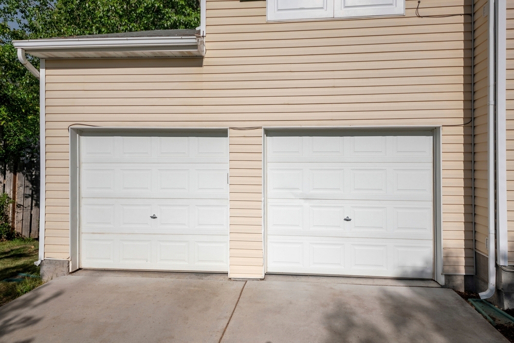 A beige house with two closed white garage doors and a concrete driveway.